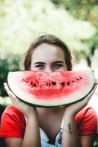 A woman holding up a watermelon in front of her face and smiling