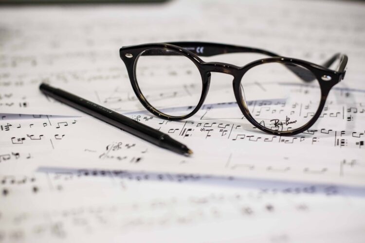 black glasses and pen sitting on sheet music