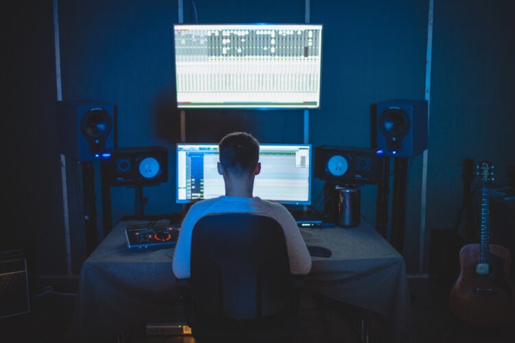 Man sitting in the dark in front of 2 computer monitors that are lit up