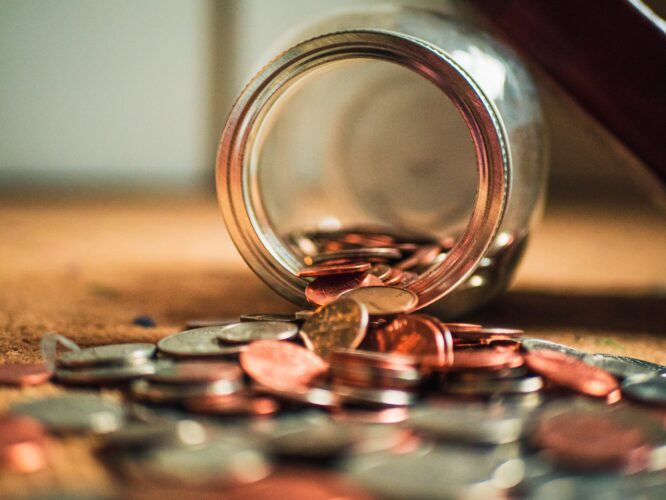 A jar of change spilling out onto a table. Money for a Cheap Harmonica.