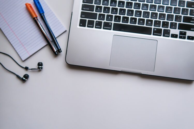 Silver laptop sitting on table next to notepad and pens