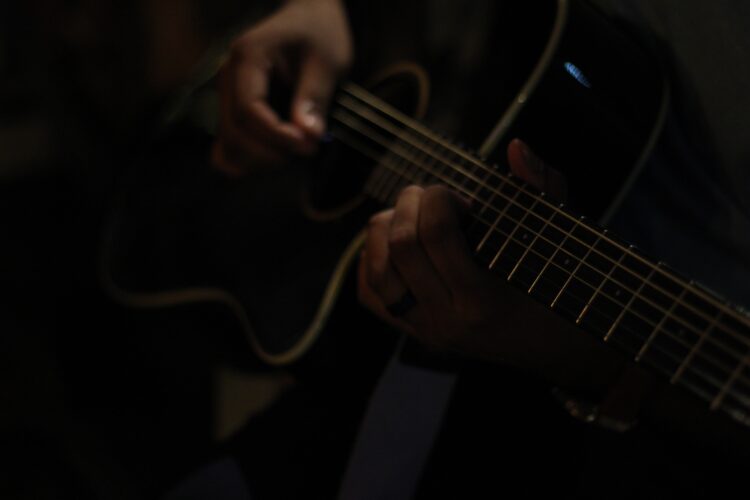 a dark image of a person strumming a guitar in a band