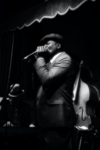 black and white photo of man playing harmonica into bullet mic